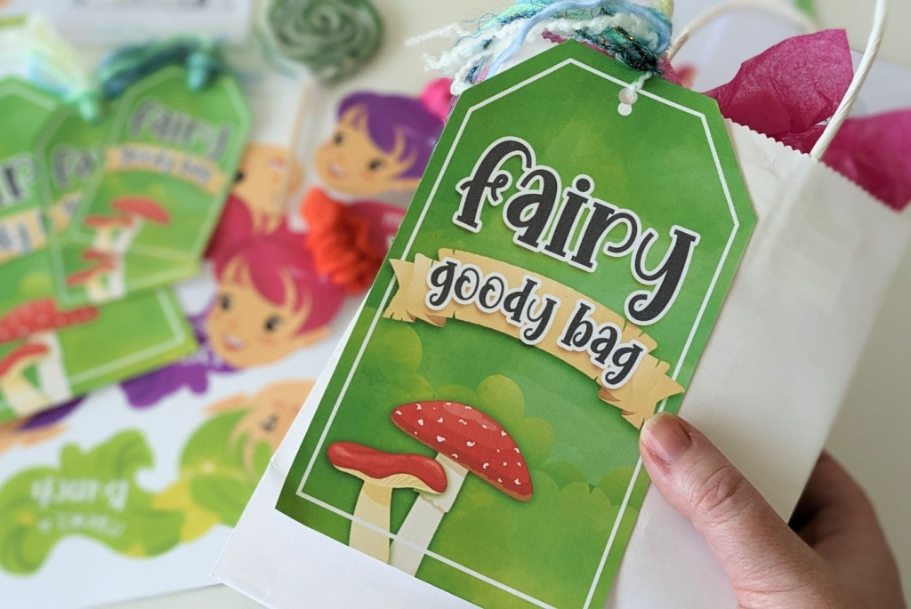 A white gift bag filled with pink tissue paper adorned with an oversized Fairy goody bag gift tag.