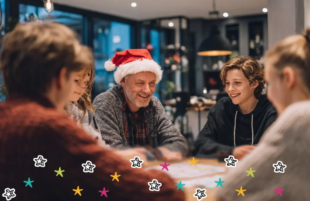 A family sat around a table playing a Christmas escape room game. Dad is wearing a red Christmas hat. 