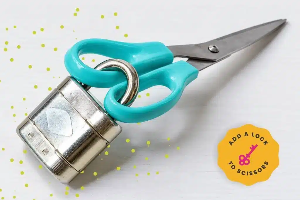 Silver padlock threaded through the Tiffany blue handles of a pair of scissors, creating a simple DIY escape room puzzle.