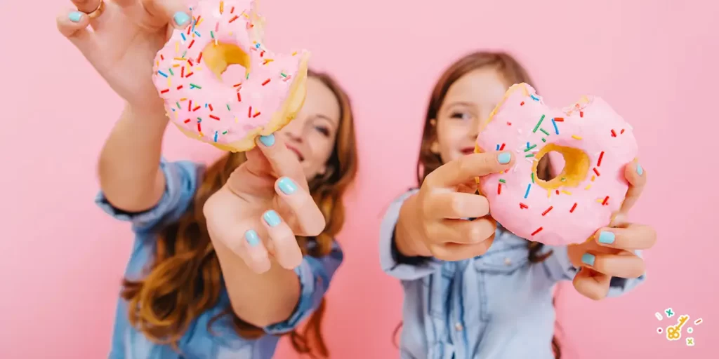 Mum and daughter holding pink donuts with sprinkles.