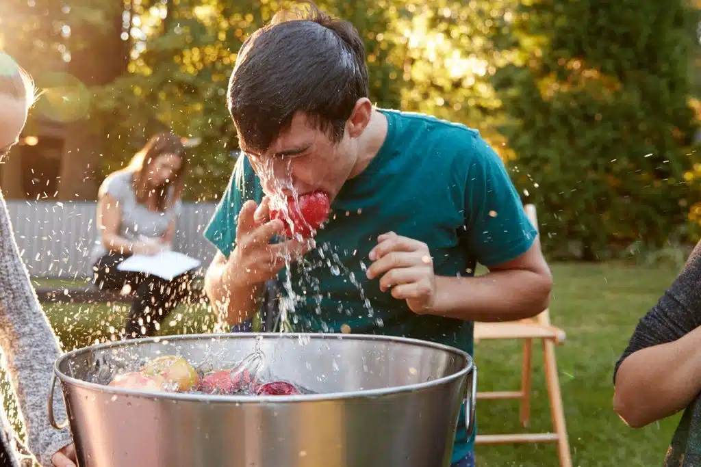 A boy bobbing for apples in a large metal bucket.