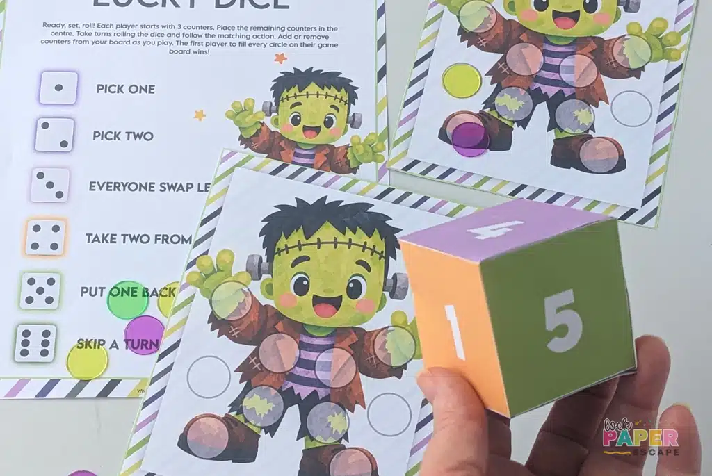 Halloween Lucky Dice printable game showing a player rolling a colorful paper die beside Frankenstein game boards, dice instructions, and counters.
